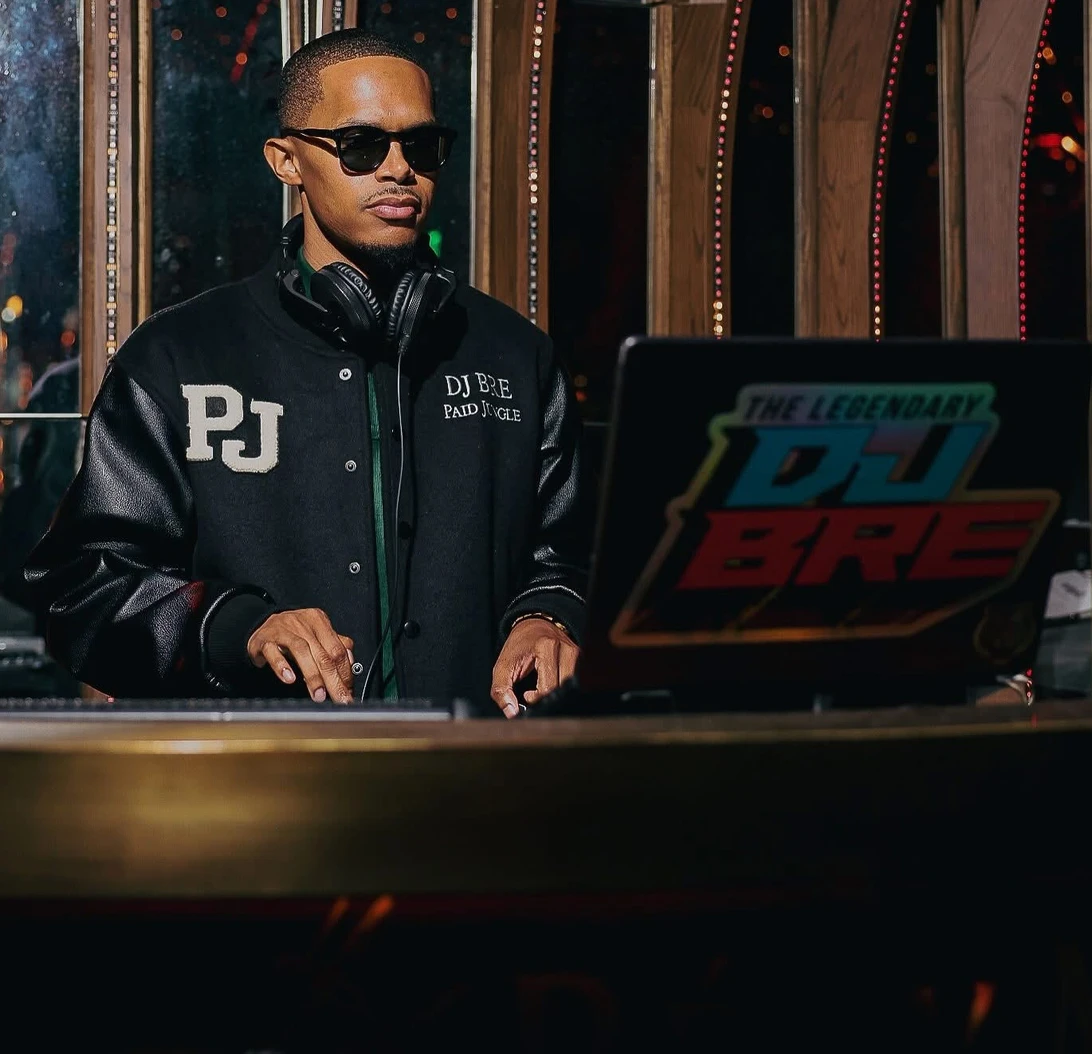 DJ BRE wearing a Paid Jungle jacket behind the DJ booth