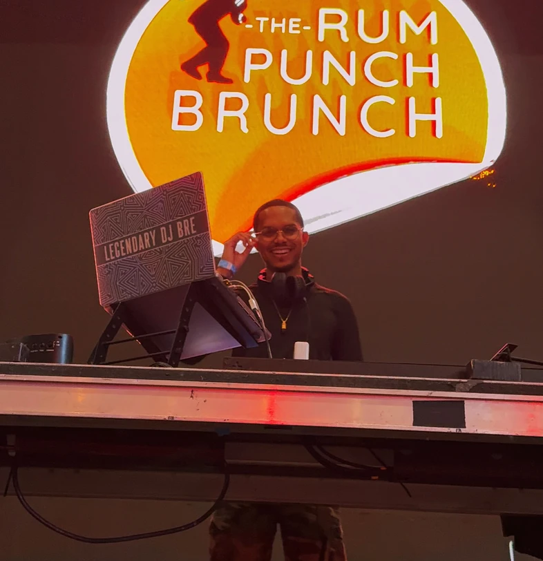 DJ BRE smiling behind the booth at the Rum Punch Brunch